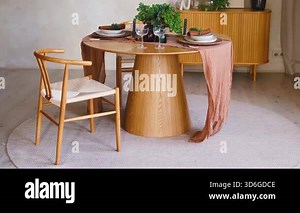 Elegant wooden dining table set with chairs and delicate pink runner in bright room