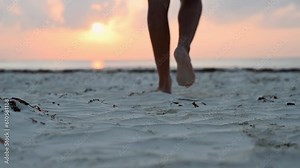 Young man walking barefoot on a sandy beach on the ocean, in the morning at sunrise. Bare legs of an adult male. Summer vacation. Slow motion.