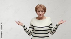 An elderly woman with a puzzled face and shocked gaze shrugs, turns a head, spreads arms and palms to the sides, shows emotions of abashment, confusion and bewilderment. Gesture of perplexity, symbol
