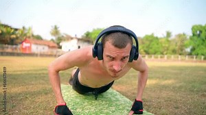 A skinny guy with a bare torso does push-ups off the floor.