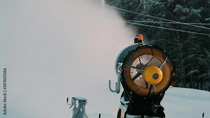 Snow making system. A snow cannon sprays water and makes snow. In the background are mountains and winter forest. Snow-making systems.