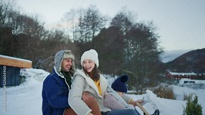 Happy young family on winter holiday with small child sledding outdoors in snowy nature.