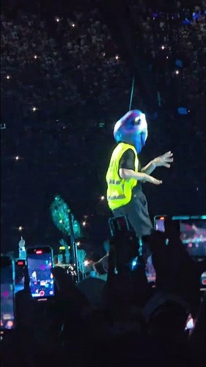 Dancer wears a vest and alien mask and dances on stage at the Coldplay concert as a gestur