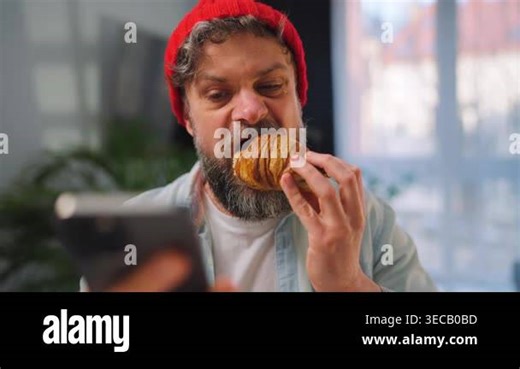 A caucasian man enjoying a fresh croissant for breakfast and using his smartphone at the same time. Modern lifestyle, scrolling social media feed, internet addiction. Slow motion Stock Video Footage - Alamy