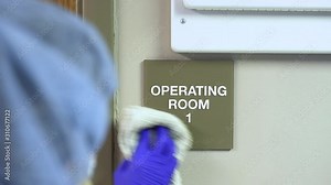 Female janitor cleaning brail sign for operating room 1 in hospital doctors office and sanitizing the sign