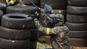 Portrait of cheerful adult people playing paintball on the battlefield. Special protective mask for playing war. Paintball player aiming.