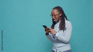 Happy excited model using online app on smartphone, browsing social media internet website and feeling positive about text messages. Cheerful smiling person showing excitement in studio.