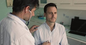 In medical examination room male cardiologist places stethoscope against patients chest, listening heartbeat, assessing rate and rhythm. Cardiovascular and heart disease prevention, regular check-up