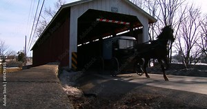 An Amish horse cart travels through a covered bridge along a road in rural Pennsylvania.