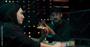A group hackers organize an attack on data servers. Their hideout is dark and full of operational displays. The guys are taking a break, eating pizza and analyzing the malware code on the computer.