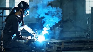 Female welder performing welding tasks in an industrial workshop in the evening