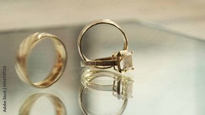 Close-up of gold and diamond rings on a glass surface, with reflections highlighting the intricate design, rings spin with beautiful reflection