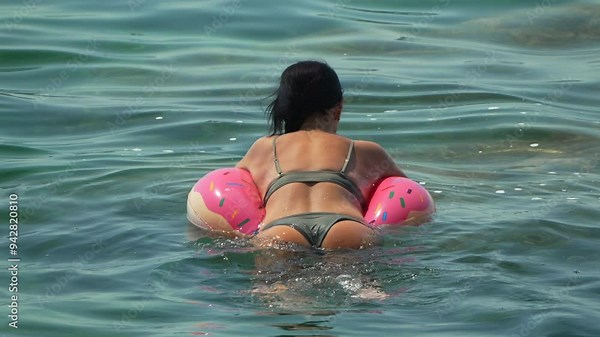 Woman Swimming Inflatable Floats Ocean on a pink donut-shaped inflatable Stock Video