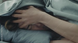 Close-up of the face of a woman who lies in bed, her head is hidden under the covers. Sleepless young woman suffering from insomnia or nightmares. Tired woman closes her eyes with her hands.