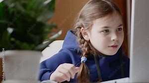 Portrait of a little girl sitting in front of a laptop, reading an article with interest, running her eyes over the lines, moved close to the computer screen.