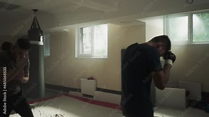 Professional trainer in boxing gear shows students basic fighting exercises in dark gym. Group sports activities and mentor improving men skills