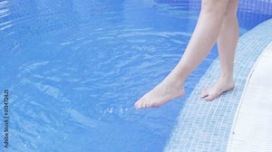 Women's feet by the pool. Woman wets feet in pool, checks water temperature