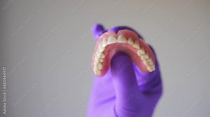 Dentist with purple gloves holding dentures in hand. Concept of dental prosthesis and dental health. Stock Video