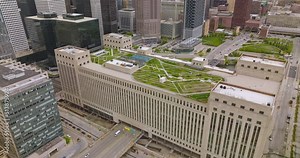 Wide multi-storied building in Chicago with beautiful green zone on the roof. Road going through the structure. Parking lot at foreground.