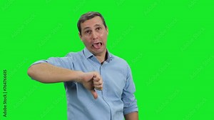 Thumb down sign gesture by young adult man expressing discontent disapproval dislike and disgust on green screen