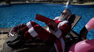 Humorous fun concept: Santa Claus are working use the laptop and hides the screen from inflatable ring, open and close computer and looking at flamingo. Summertime recreation at swimming pool area