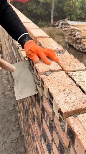 building the orange brick wall on the ground using cement and a metal trowel for the construction