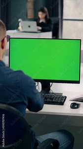 Young Man Working At Computer With Green Mock Up Screen in Office. Close Up Desktop Computer Monitor with Mock Up Green Screen Chroma Key Display. Vertical Video