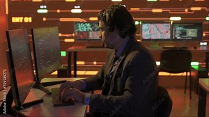 Technical support in control room. Man IT specialist works on computer in headset at the office, big digital screen shows infrastructure data.