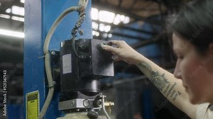 woman mechanic with tattoos presses button on hydraulic lift and lifts car for maintenance or repair in car service. Lady has her own small business and works there.