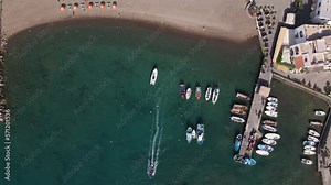 4k bird's eye view drone shot of a beautiful beach with boats leaving port on the island of Ischia in Italy. This port is located on the Southside of the island in Sant Angelo.