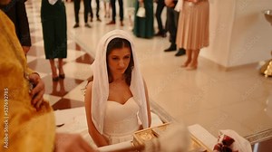 woman kneels praying with head covered in headscarf priest blesses bride sprinkled her Sacred water Newlyweds groom get married holy father in church. worship divine service church chapel ministration