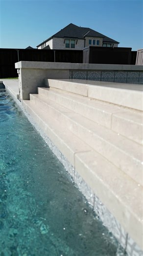 This custom design features a raised spa with a cascading, tiered spillway that flows beautifully into the main pool — creating the perfect visual and soothing sound. The spacious tanning ledge, complete with gentle bubblers, offers the ideal place to unwind and soak up the sun. Check out our galleries at the link for all the backyard inspo you need to start dreaming big! 🌴💦 https://emeraldcustompools.com #emeraldcustompools #dfwpools #custompooldesign #luxurypools #backyardoasis #poolgoals #p