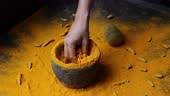 Woman hand powdering Indian spices turmeric powder stone mortar...