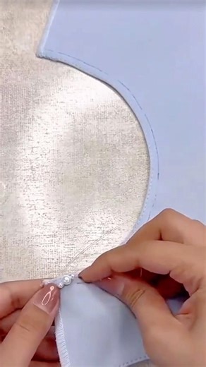 Hand-Sewing Decorative White Pearls onto the Edge of a Light Blue Garment