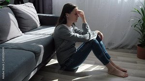 Unhappy young woman thinking about problems, sitting on floor in living room alone, frustrated depressed female feeling lonely and sad, suffering from bad relationship, break up or divorce concept