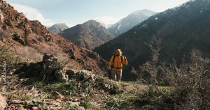 Epic inspiring video of motivating male hiker during exploration camping trip climbs up mountain ridge in incredible natural landscape on sunny day. Cinematic, taking in scenic views of mountains