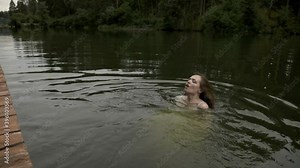 A young woman bathes in her clothes in the cold water of a deserted forest lake
