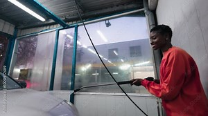 Smiling African American woman washing her car at self-service car wash. Embracing independence and practicality, female takes care of routine tasks with a smile. everyday responsibility