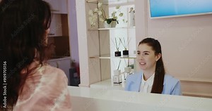 A professional receptionist greets a customer with a friendly smile in a stylish, pastel-themed reception area. The setting exudes warmth and professionalism, enhancing customer service.