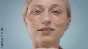 front view portrait of young blonde model in undereye patches watching to the camera, then touches undereye zone