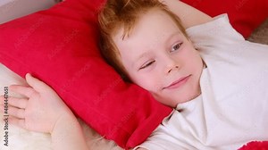 Morning in bed kids. Cute funny cheerful little boy wakes up and lies in bed in the morning, stretches and smiles. 4k video clip. Relaxation in bed.