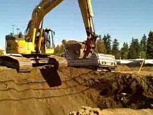 A Giant Track Hoe Digging A Hole In The Dirt At A Construction Site Building A New Apartment