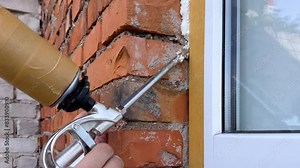 Installation of a window. The process of insulating windows with construction foam. A builder's hand seals the gaps between the building and the window frame. Window insulation in a building.