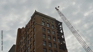 A detailed view of the demolition process of a historic high-rise building in Youngstown, Ohio. The crane with a wrecking ball is seen actively dismantling the ornate upper structure.