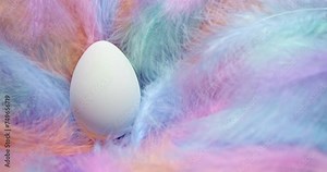 Soft fluffy pastel feathers blowing in the wind with a single white Easter Egg. Gentle Easter theme with egg in delicate nest of feathers.