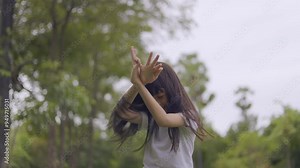A cute kid girl is playing a butterfly dance and flying in the middle of the garden by joining her hands to make wings like a butterfly, having fun in the midst of nature in the shady green garden.