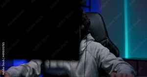 A view of a boy playing computer games talking to a band through a headset from behind monitors, a dark room lit by led lights.