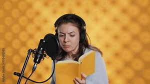 Woman does voiceover reading of book to produce audiobook using dramatic acting. Narrator uses storytelling skills and expressive sounds while producing recording of novel, studio background, camera A