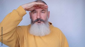 Mature bearded man looking through binoculars with surprised expression and thumbs up. Successful search concept. Internet search engine. Grey background.