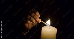 Old religious woman igniting match and putting on candle in a dark space - wide Stock Video